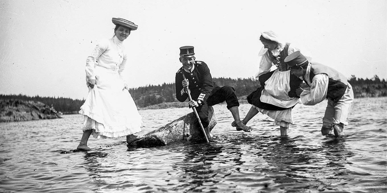 En man och tre kvinnor badar fötterna i en sjö