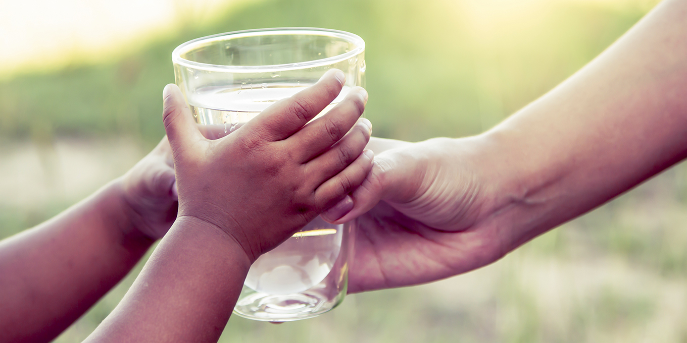 Barnhänder tar emot vattenglas från vuxen