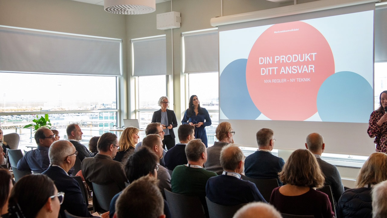 Ett stort rum där människor sitter och lyssnar på en presentation